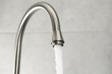 Photo of Water saving concept. Stream of water flowing from tap indoors, closeup