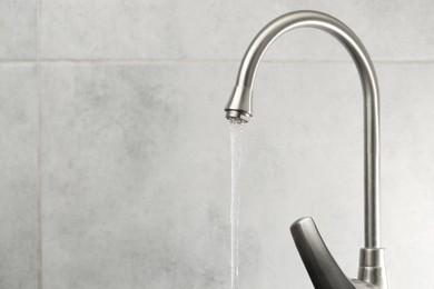 Photo of Water saving concept. Stream of water flowing from tap indoors, closeup. Space for text