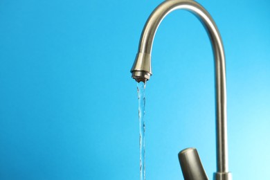 Photo of Water saving concept. Stream of water flowing from tap on light blue background, closeup. Space for text