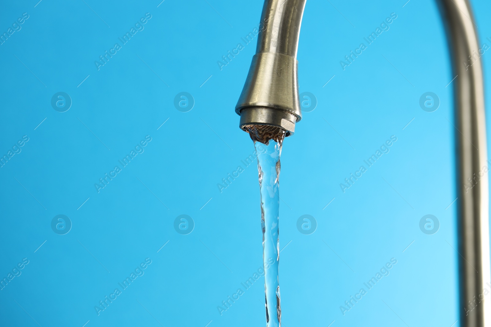 Photo of Water saving concept. Stream of water flowing from tap on light blue background, closeup. Space for text