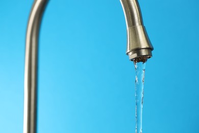 Photo of Water saving concept. Stream of water flowing from tap on light blue background, closeup