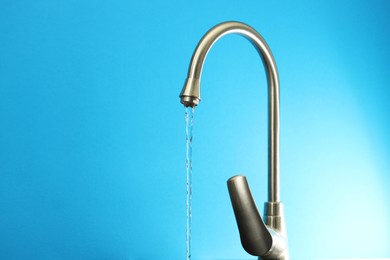 Photo of Water saving concept. Stream of water flowing from tap on light blue background, closeup. Space for text