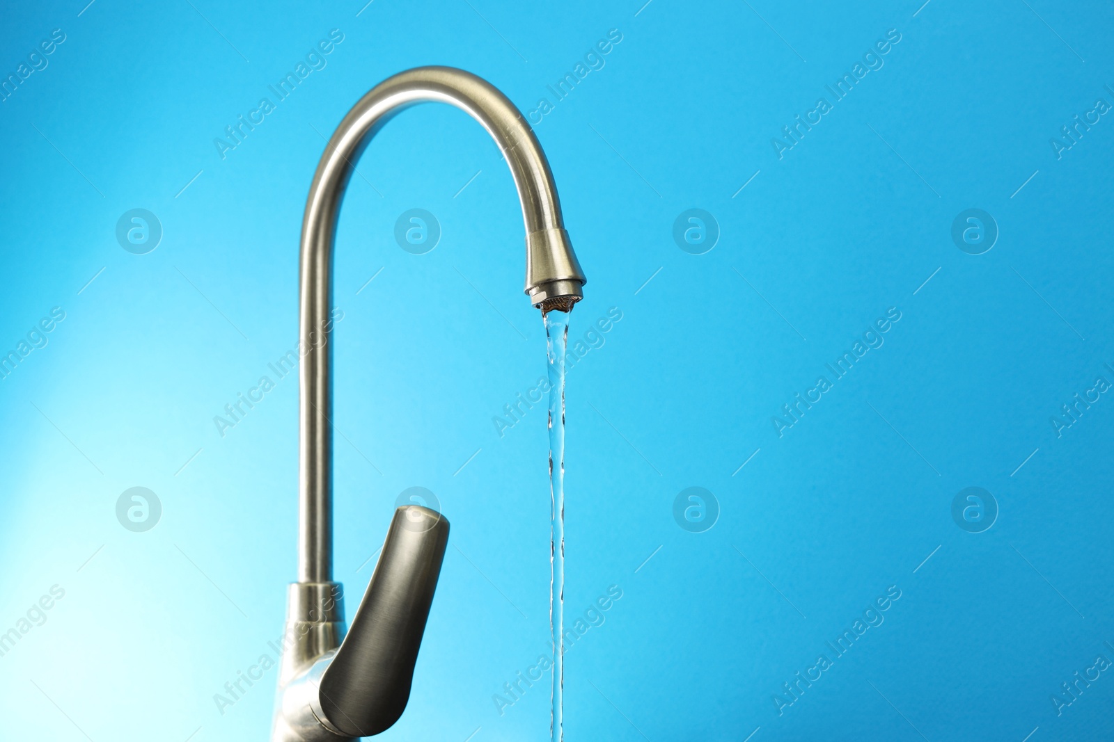 Photo of Water saving concept. Stream of water flowing from tap on light blue background, closeup. Space for text