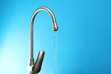 Photo of Water saving concept. Stream of water flowing from tap on light blue background, closeup. Space for text