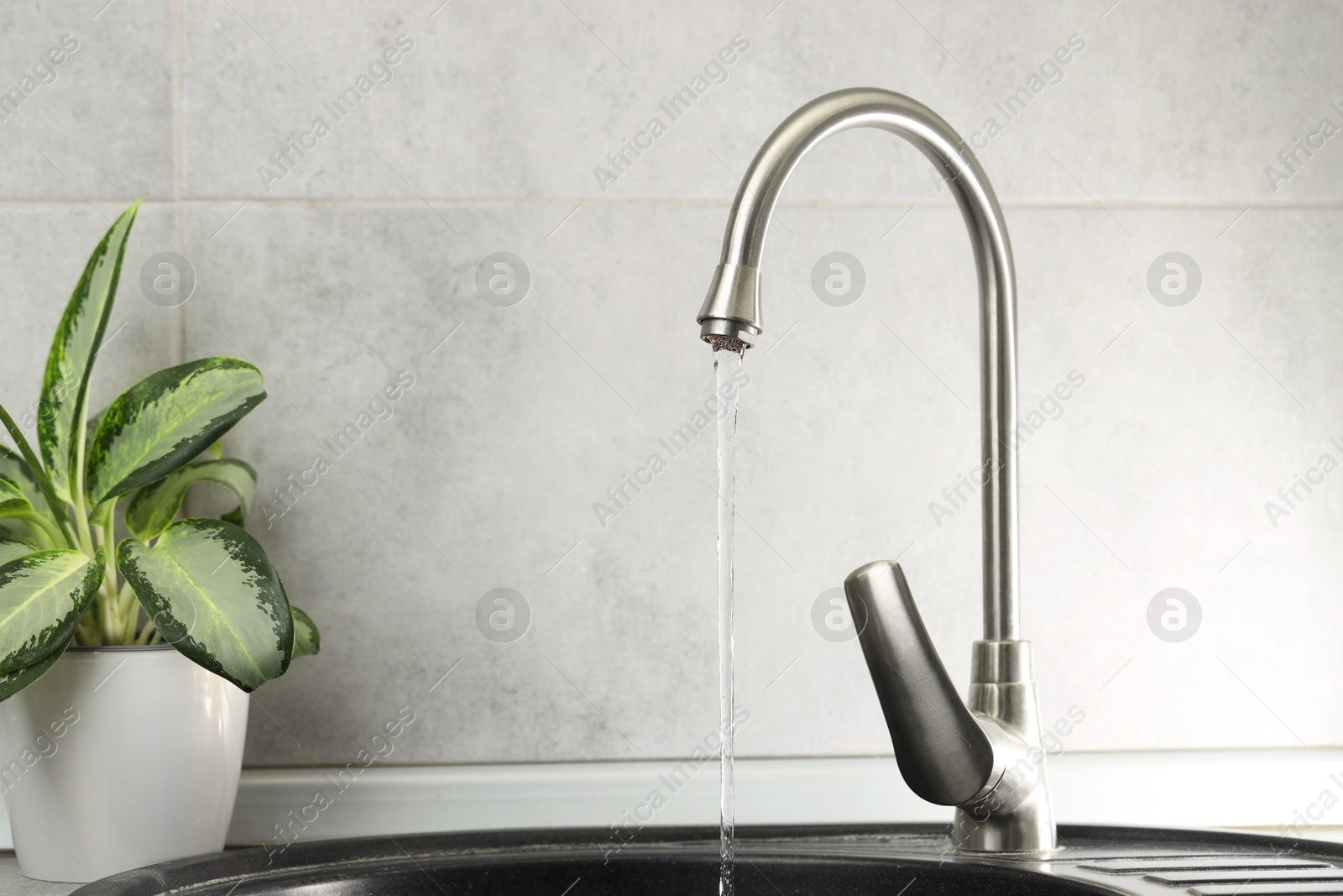 Photo of Water saving concept. Stream of water flowing from tap indoors, closeup