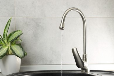 Photo of Water saving concept. Stream of water flowing from tap indoors, closeup