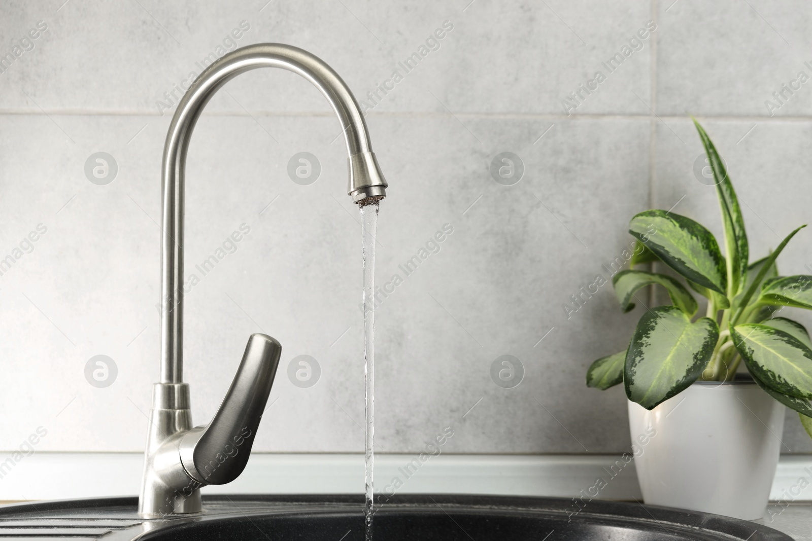 Photo of Water saving concept. Stream of water flowing from tap indoors, closeup