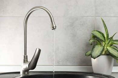 Photo of Water saving concept. Stream of water flowing from tap indoors, closeup