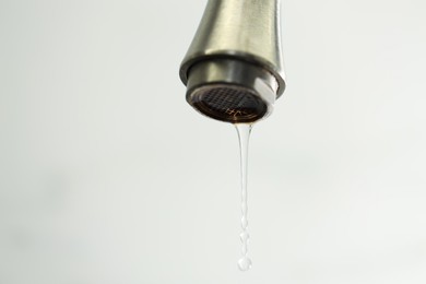Photo of Water saving concept. Water dripping from tap on light background, closeup