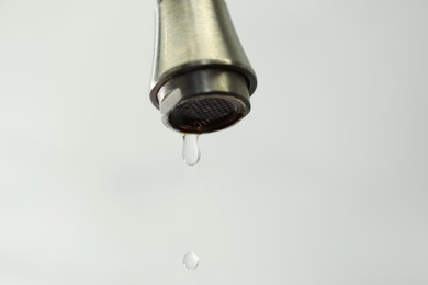 Photo of Water saving concept. Water dripping from tap on light background, closeup