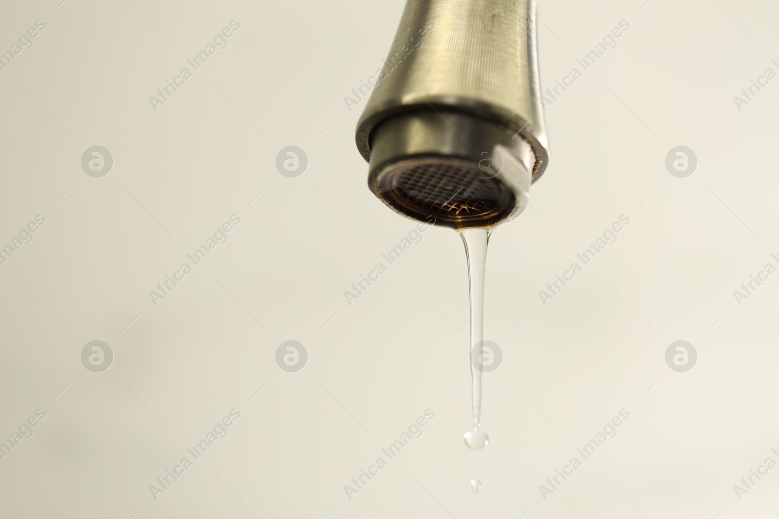 Photo of Water saving concept. Water dripping from tap on light background, closeup