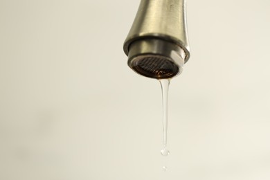 Photo of Water saving concept. Water dripping from tap on light background, closeup