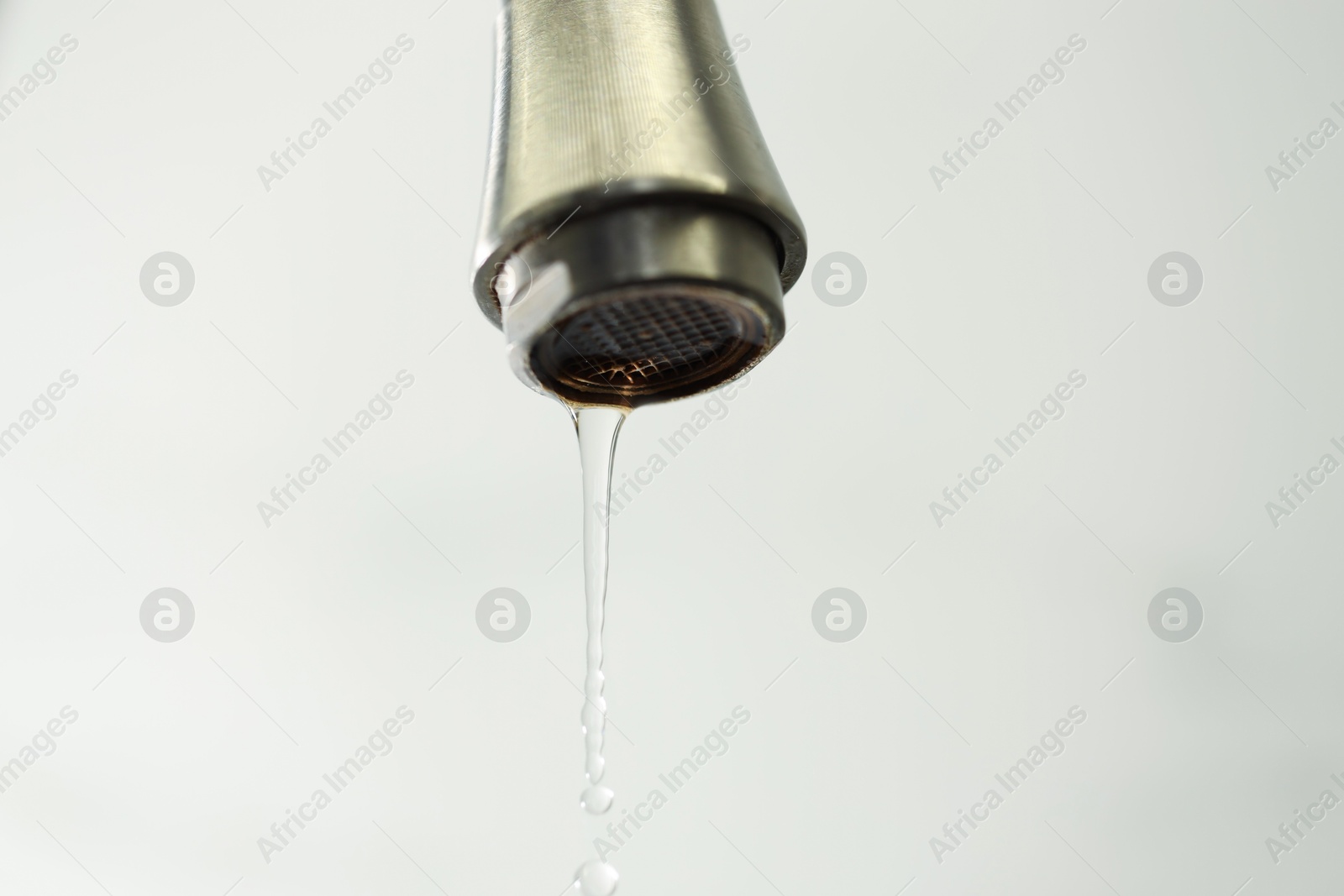 Photo of Water saving concept. Water dripping from tap on light background, closeup