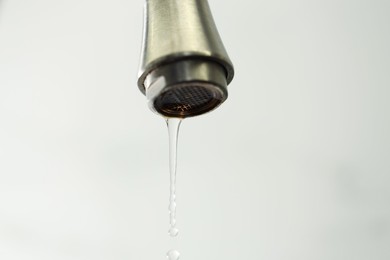 Photo of Water saving concept. Water dripping from tap on light background, closeup
