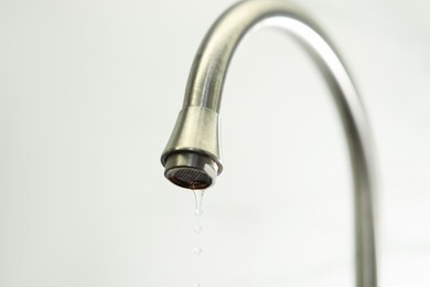 Photo of Water saving concept. Water dripping from tap on light background, closeup