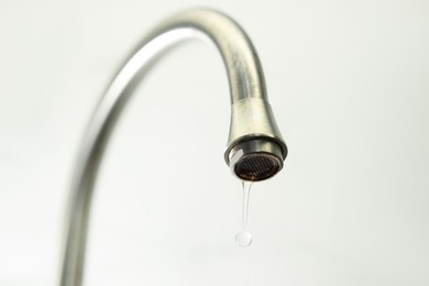 Photo of Water saving concept. Water dripping from tap on light background, closeup
