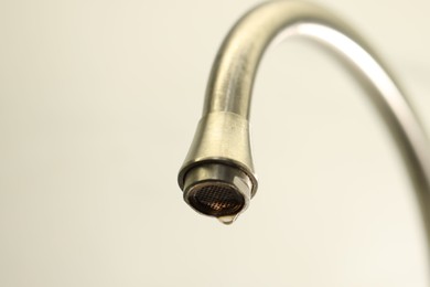 Photo of Water saving concept. Water dripping from tap on light background, closeup