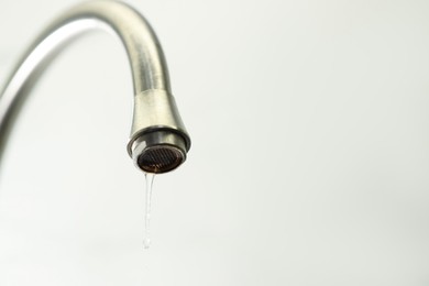 Photo of Save water concept. Water dripping from tap on light background, closeup. Space for text