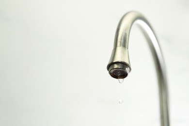 Photo of Save water concept. Water dripping from tap on light background, closeup. Space for text