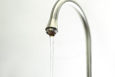 Photo of Water saving concept. Stream of water flowing from tap on light background, closeup