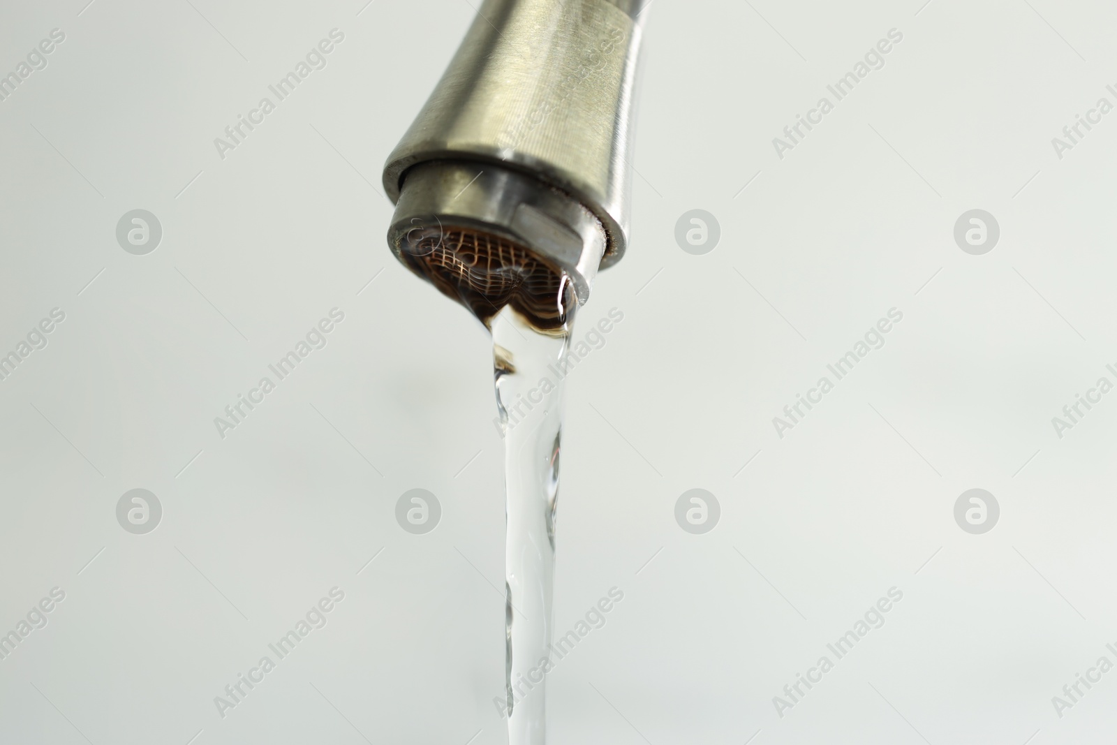 Photo of Water saving concept. Stream of water flowing from tap on light background, closeup