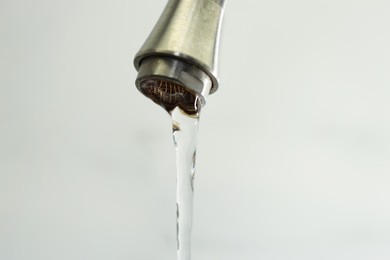 Photo of Water saving concept. Stream of water flowing from tap on light background, closeup