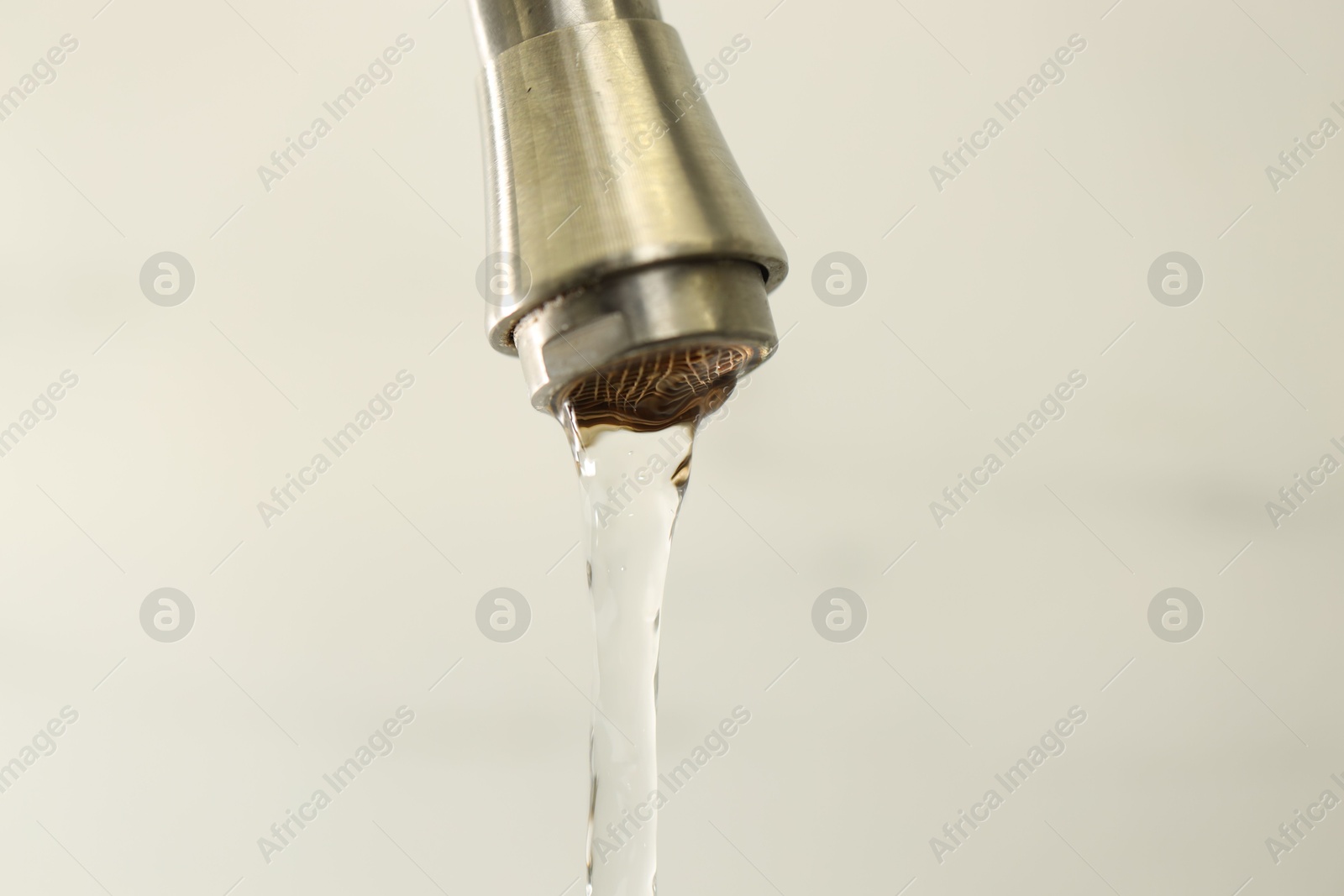 Photo of Water saving concept. Stream of water flowing from tap on light background, closeup
