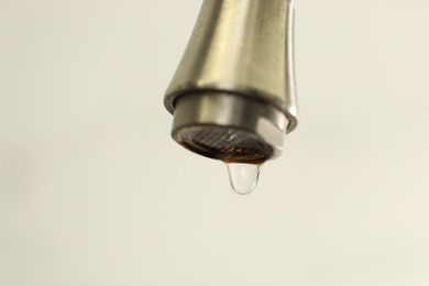 Photo of Water saving concept. Water dripping from tap on light background, closeup