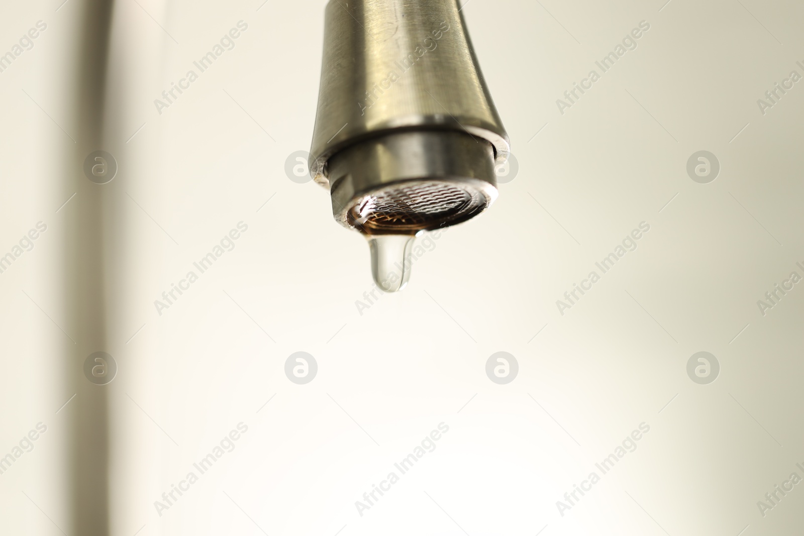 Photo of Water saving concept. Water dripping from tap on light background, closeup
