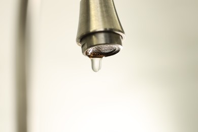Photo of Water saving concept. Water dripping from tap on light background, closeup