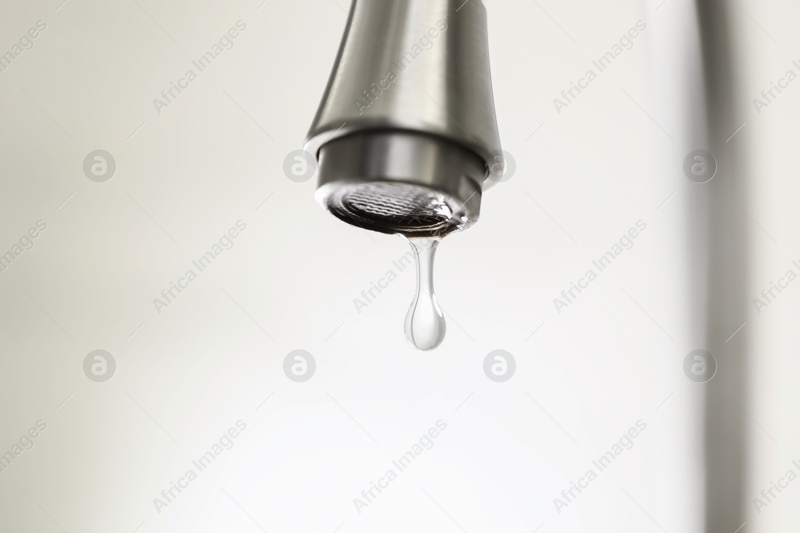Photo of Water saving concept. Water dripping from tap on light background, closeup