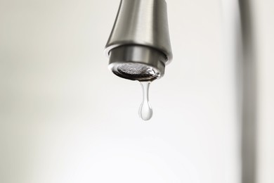 Photo of Water saving concept. Water dripping from tap on light background, closeup