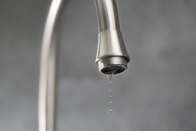 Photo of Save water concept. Water dripping from tap on grey background, closeup
