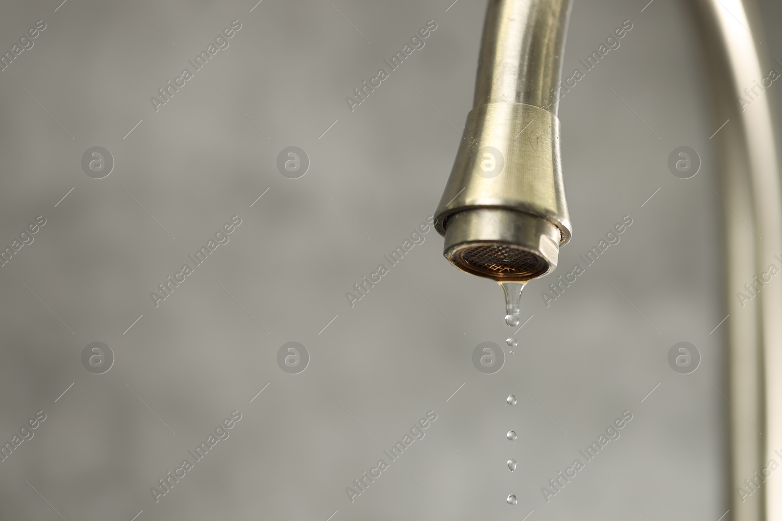 Photo of Water saving concept. Water dripping from tap on grey background, closeup. Space for text