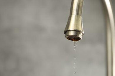 Photo of Water saving concept. Water dripping from tap on grey background, closeup. Space for text