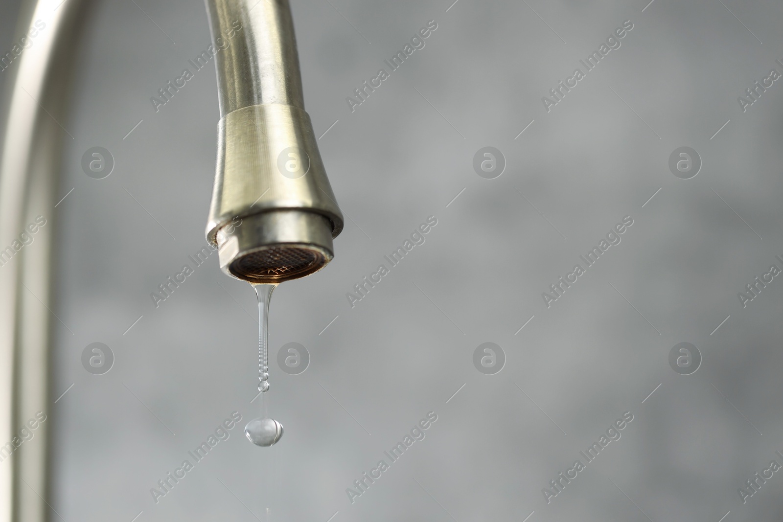 Photo of Water saving concept. Water dripping from tap on grey background, closeup. Space for text