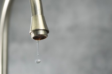Photo of Water saving concept. Water dripping from tap on grey background, closeup. Space for text