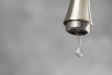 Photo of Water saving concept. Water dripping from tap on grey background, closeup. Space for text