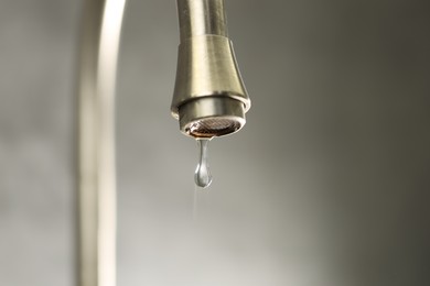Photo of Water saving concept. Water dripping from tap on grey background, closeup. Space for text