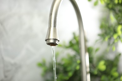 Photo of Water saving concept. Stream of water flowing from tap indoors, closeup