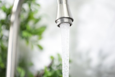 Photo of Water saving concept. Stream of water flowing from tap indoors, closeup