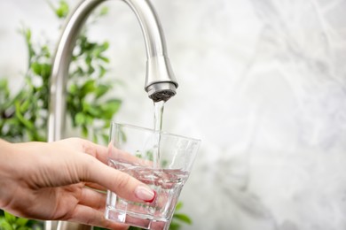 Photo of Water saving concept. Woman filling glass with tap water indoors, closeup. Space for text