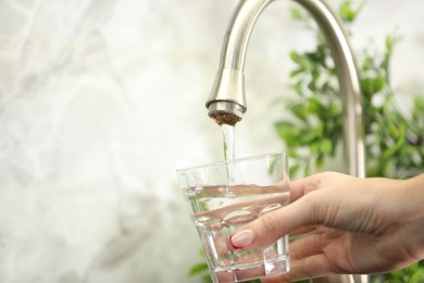 Photo of Water saving concept. Woman filling glass with tap water indoors, closeup. Space for text