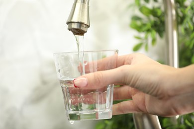 Photo of Water saving concept. Woman filling glass with tap water indoors, closeup