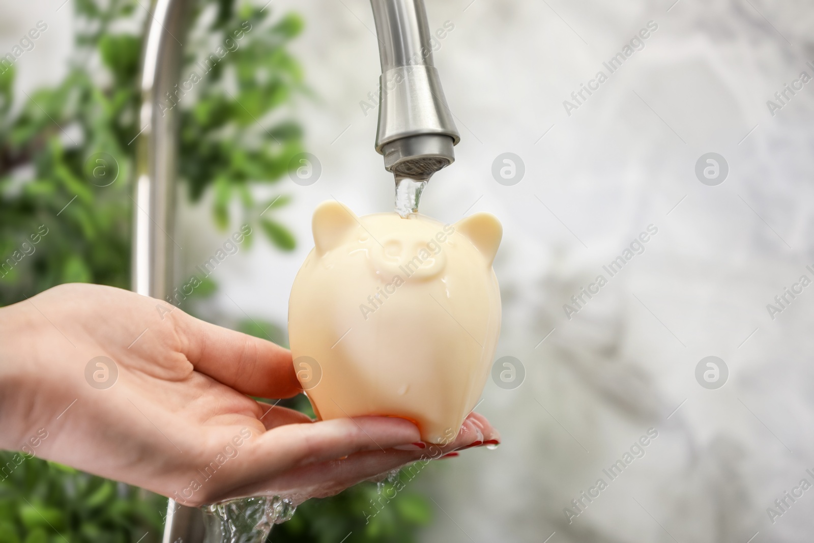 Photo of Water saving concept. Woman holding piggy bank under tap indoors, closeup