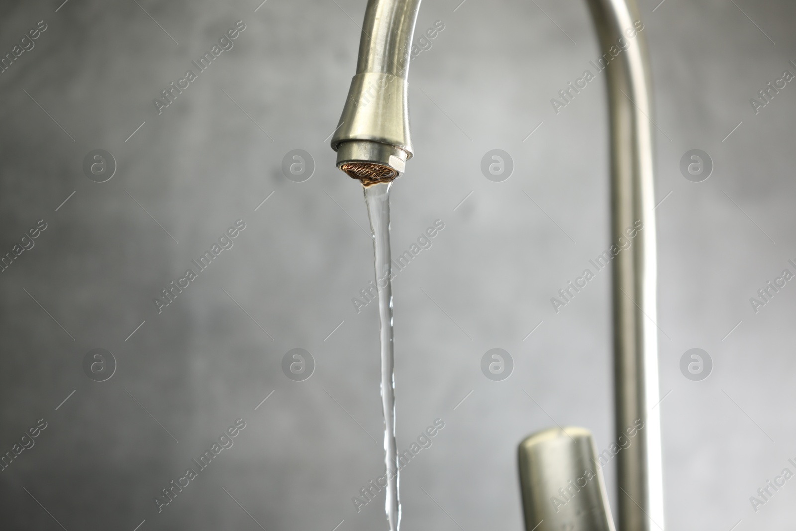 Photo of Save water concept. Stream of water flowing from tap against grey background, closeup