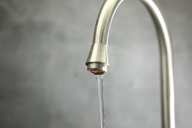 Photo of Save water concept. Stream of water flowing from tap against grey background, closeup. Space for text