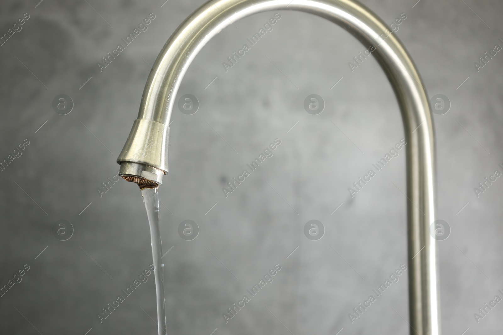 Photo of Save water concept. Stream of water flowing from tap against grey background, closeup