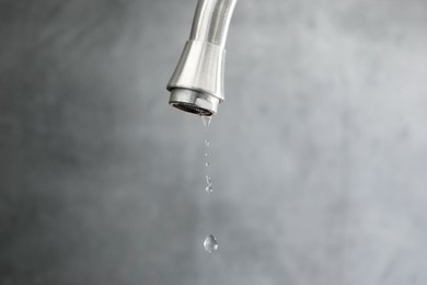 Photo of Save water concept. Water dripping from tap against grey background, closeup