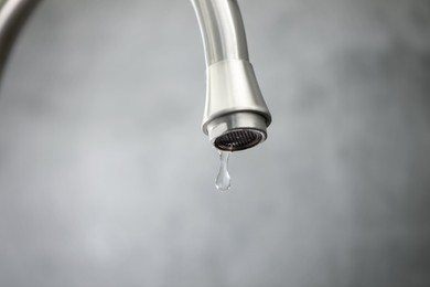 Photo of Save water concept. Water dripping from tap against grey background, closeup